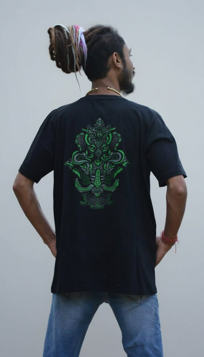 Person wearing a black t-shirt with a green design on the back, standing in a forest.