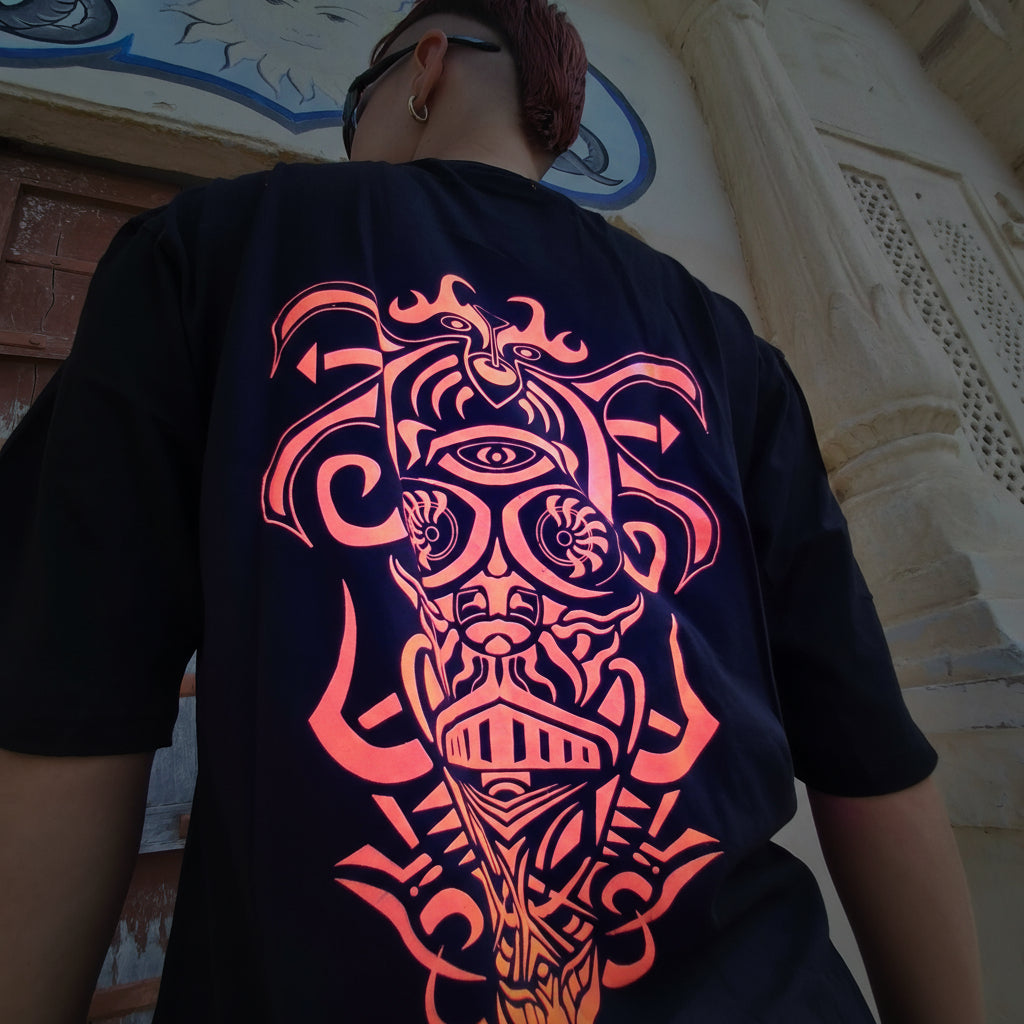 Person wearing a black t-shirt with orange tribal design, standing against a stone wall.