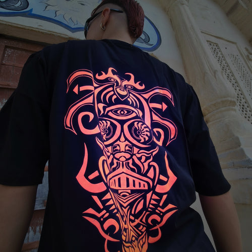 Person wearing a black t-shirt with orange tribal design, standing against a stone wall.